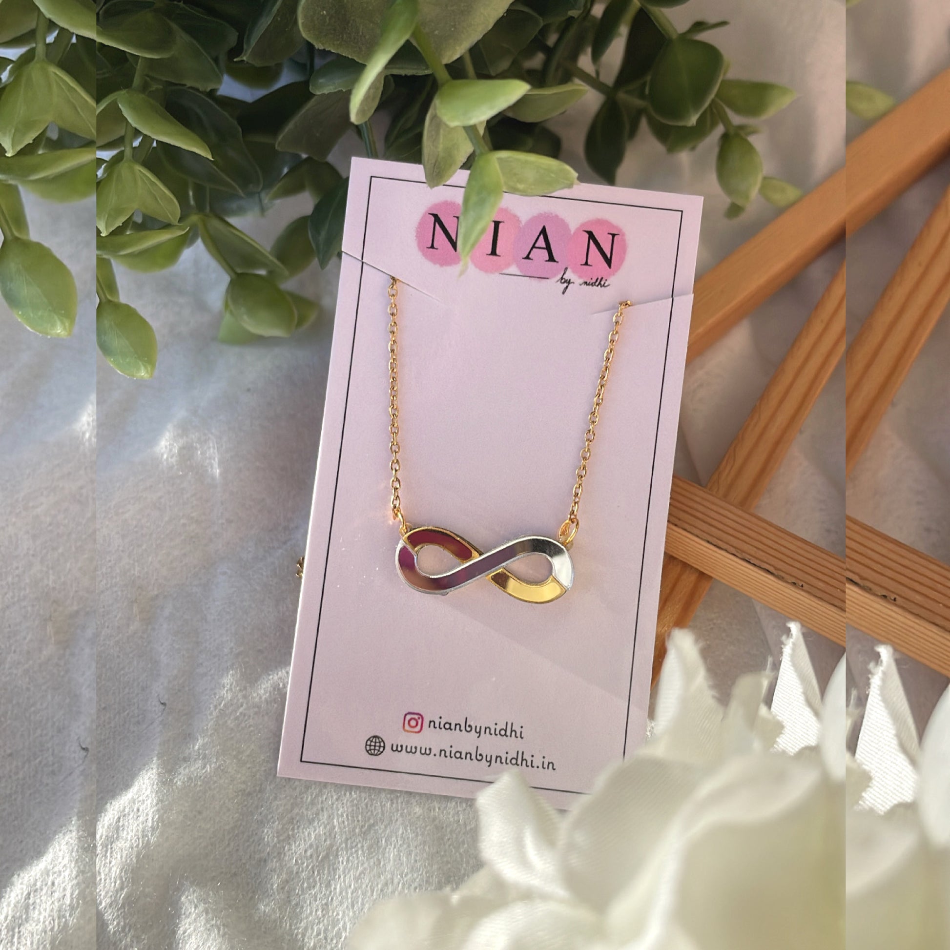 Infinity Necklace - Glossy Golden and Silver - Nian by Nidhi - placed in a white and green background