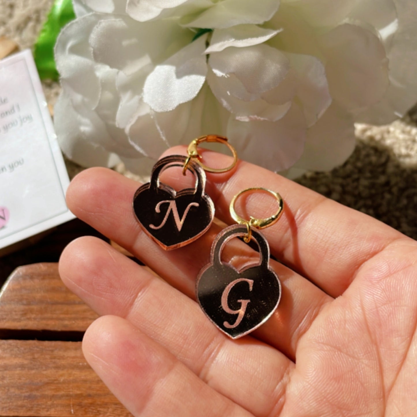 Initial Heart Lock Earrings - Glossy Rosegold - Nian by Nidhi - placed on a hand in a white and brown background